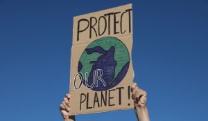 Two hands holding a placard with words 'Protect Our Planet' and picture of earth with colours blue and green drawn in the centre